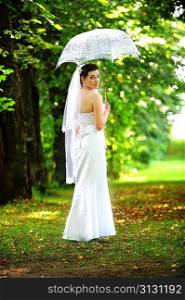 beautiful bride with umbrella walking in park