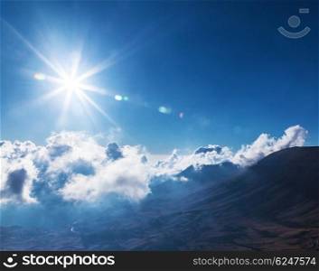 Beautiful bright sun in blue cloudy sky over high mountains, stunning cloudscape, natural background, fresh air, summer time