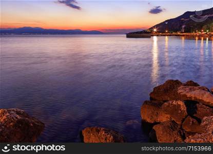 Beautiful, bright sunset on the Corinthian bay, cityscape promenade in the night city of Loutraki in Greece.. Beautiful, bright sunset on the Corinthian bay at night Loutraki, Greece.