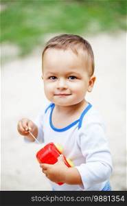 Beautiful brown-eyed little boy playing with a red plastic toy car outdoors