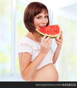 Beautiful brunet pregnant woman eating red ripe watermelon, spending time at home, happy healthy pregnancy