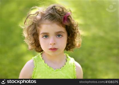 Beautiful brunette blue eyes little girl portrait on the park green grass