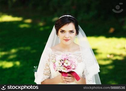 Beautiful brunette bride with bouquet outdoor. Happy bride outdoors. Beautiful bride posing in her wedding day