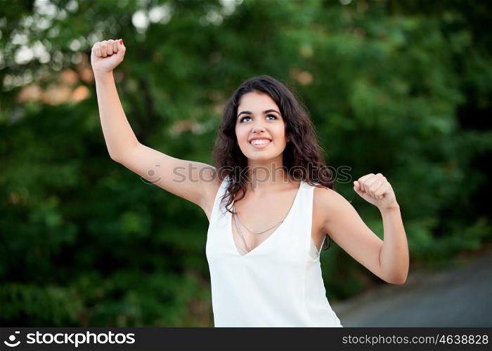 Beautiful brunette girl celebrating something in the park wiht many plants of background