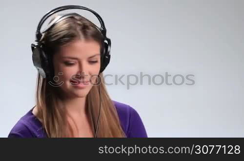 Beautiful brunette girl in black stylish headphones enjoying music on white. Cheerful young lady having fun, making funny facial expressions, gesturing and showing heart sign in the air by her hands while listening to the upbeat song in earphones.