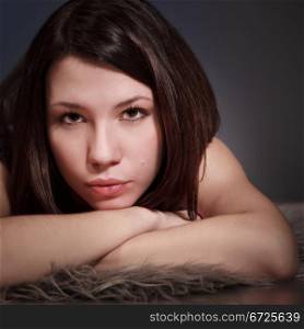 beautiful brunette girl portrait, serious, laying on fur