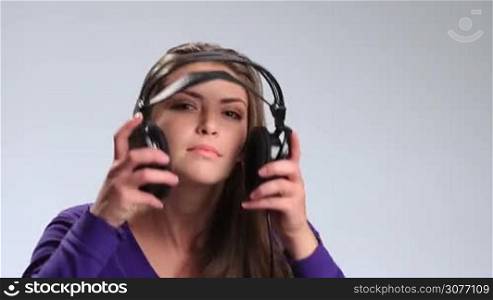 Beautiful brunette girl putting headphones on and enjoying the music on white. Cheerful young woman with both hands on earcups listening to the music and tenderly smiling at the camera.
