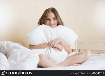 Beautiful brunette girl sitting on bed and hugging white pillow