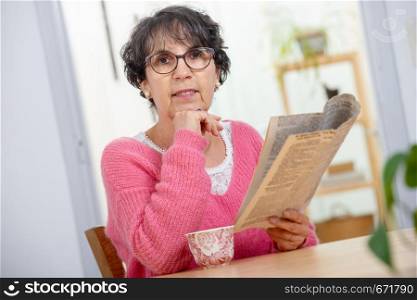 beautiful brunette mature woman dressing in pink reading a newspaper