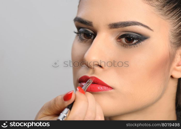 Beautiful brunette portrait, applying perfect makeup to her lips