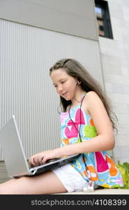 Beautiful brunette teen little girl laptop city gray background