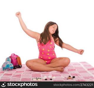 beautiful brunette teenage girl in swimsuit at the beach relaxing with arms raised (studio setting with cap, towel, bag, sun lotion, sunglasses and stones) isolated on white background