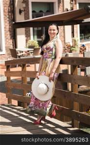 Beautiful brunette woman holding white hat and posing on old wooden bridge