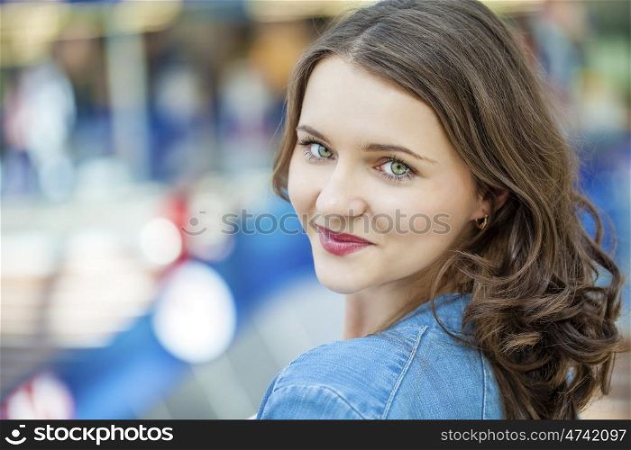 Beautiful brunette woman in blue jeans jacket, against summer street