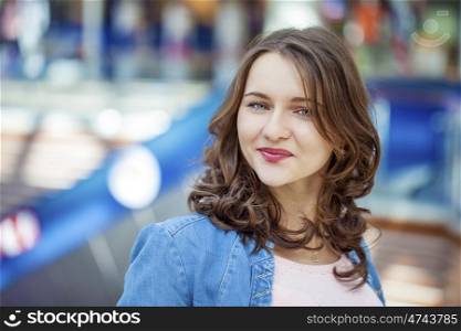 Beautiful brunette woman in blue jeans jacket, against summer street