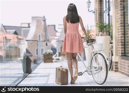 beautiful brunette woman in pink dress with bicycle and suitcase. brunette woman with bicycle