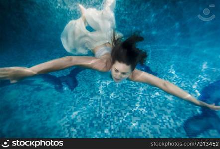 Beautiful brunette woman in white dress swimming underwater at pool