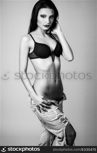 Beautiful brunette woman, model of fashion, wearing black underwear and jeans. Young girl in lingerie. Studio shot.