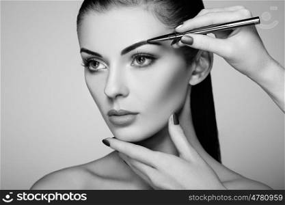 Beautiful brunette woman paints the eyebrows. Beautiful woman face. Makeup detail. Beauty girl with perfect skin. Black and White