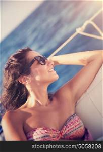 Beautiful brunette woman relaxing on sailboat, sitting on the deck and enjoying bright sun light, luxury summer vacation on water transport