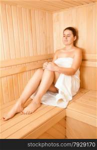 Beautiful brunette woman sitting on bench at wooden traditional sauna