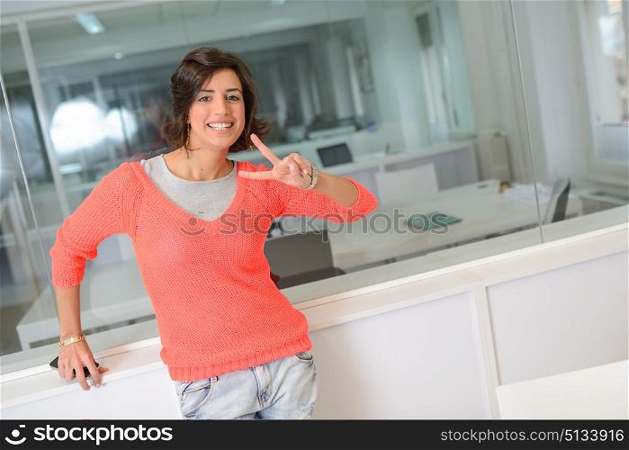 Beautiful brunette woman smiling with casual clothes in an office. Girl making a v sign