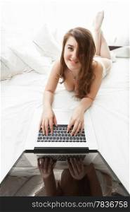 Beautiful brunette woman typing on laptop in bed