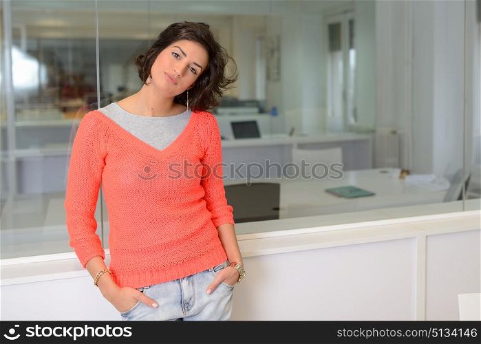 Beautiful brunette woman with casual clothes in an office. Girl wearing orange sweater and blue jeans