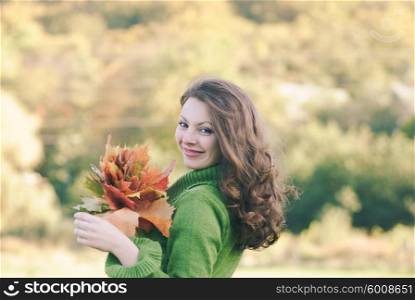 Beautiful brunette woman with maple leaves, autumnal background with copy space