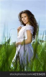 Beautiful brunette young woman in white dress on green field