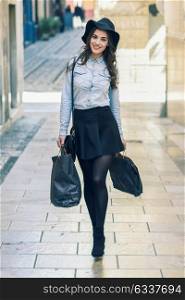 Beautiful brunette young woman wearing short skirt and denim shirt walking on the street with shopping bags