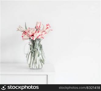 Beautiful bunch of tulips in glass vase on white table at wall. Flowers in interior design. Cozy home. Springtime