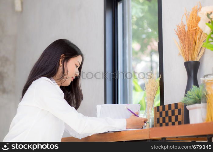 Beautiful business asian young woman writing on notebook on table, girl work at coffee shop, freelance business concept.