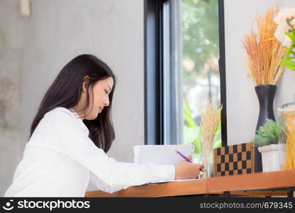 Beautiful business asian young woman writing on notebook on table, girl work at coffee shop, freelance business concept.