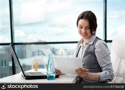 Beautiful business woman looking at papers she holding in her arms while working on computer at her office