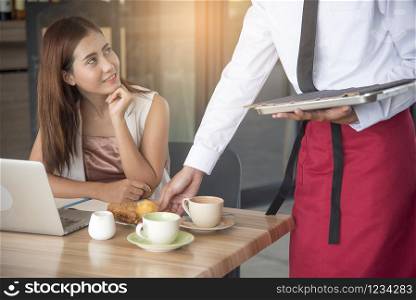 Beautiful business woman smiling looking at handsome waiter while serving food.