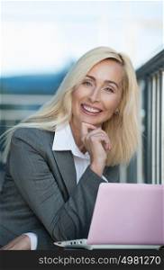 Beautiful business woman smiling while working on laptop near her office outdoor
