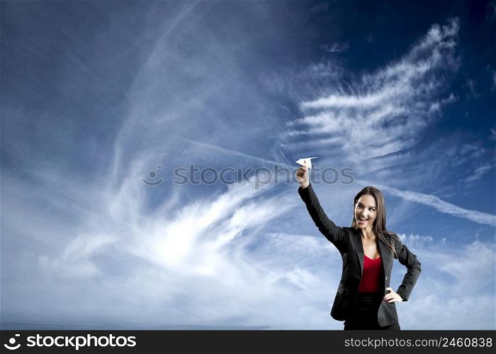 Beautiful business woman throwing a paper plane, against a beautiful blue sky