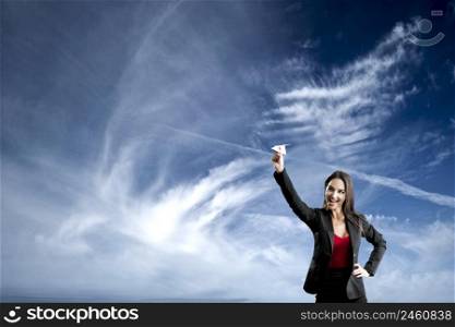 Beautiful business woman throwing a paper plane, against a beautiful blue sky