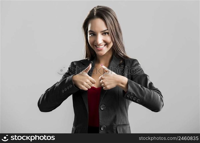 Beautiful business woman with thumbs up, over a gray background