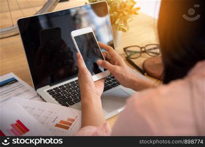 Beautiful business working woman using Iphone Ipad while working with laptop and reading report , graphs , charts, document at work. Business woman working at her desk.