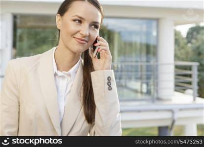 Beautiful businesswoman answering cell phone against office building