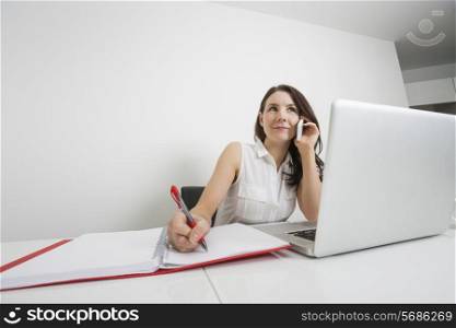 Beautiful businesswoman answering cell phone while writing at desk in office