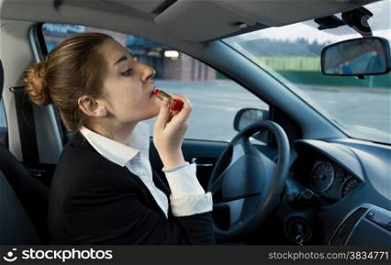 Beautiful businesswoman applying cosmetics while driving a car