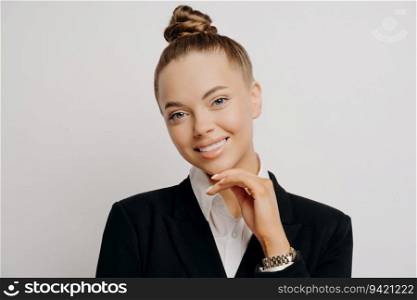Beautiful businesswoman in formal attire, confidently posing with a bun, smiling, hand on chin.