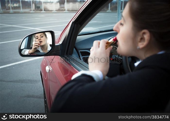 Beautiful businesswoman sitting in car and applying lipstick