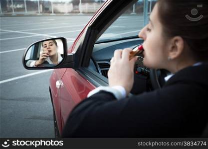 Beautiful businesswoman sitting in car and applying lipstick