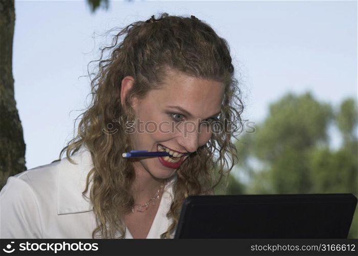Beautiful businesswoman starting to go slowly crazy while looking at her laptop, with a pencil in her mouth