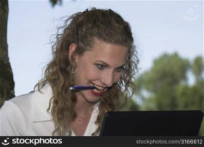 Beautiful businesswoman starting to go slowly crazy while looking at her laptop, with a pencil in her mouth