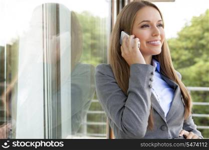 Beautiful businesswoman using cell phone by glass door